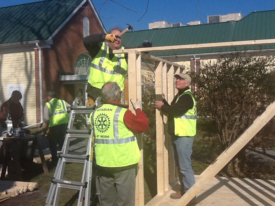 People building a wooden structure outdoors on a sunny day, wearing safety vests.