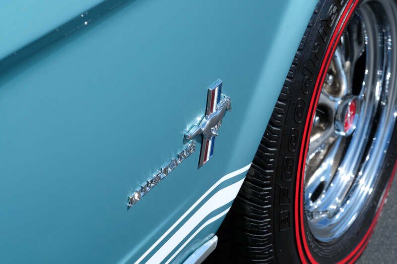 Close-up of a vintage blue Ford Mustang with chrome wheel and tire, featuring a red stripe.