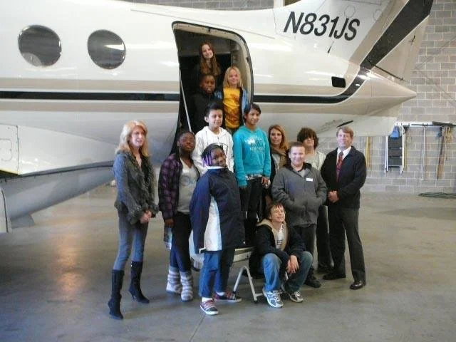 Group of people standing in front of a private jet inside an airplane hangar.