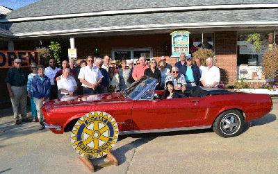Group of people standing behind a red convertible car outside a building with the Rotary logo in front.