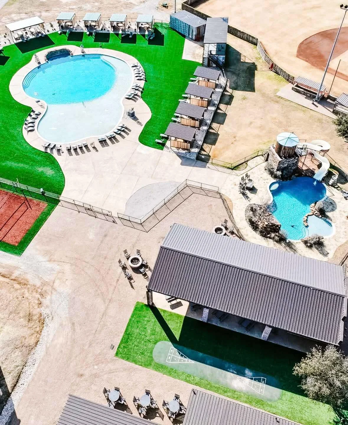 Aerial view of a swimming pool, a smaller pool or hot tub, a play area, and seating areas at an outdoor recreational facility