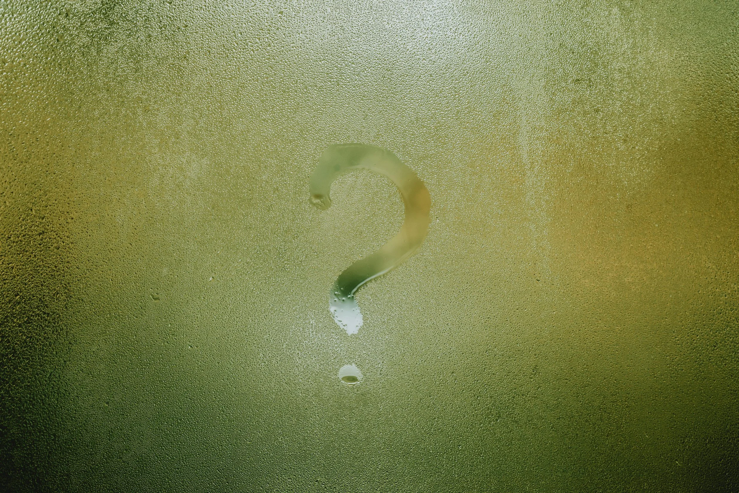 A foggy or frosted glass surface with a water droplet in the shape of a question mark.