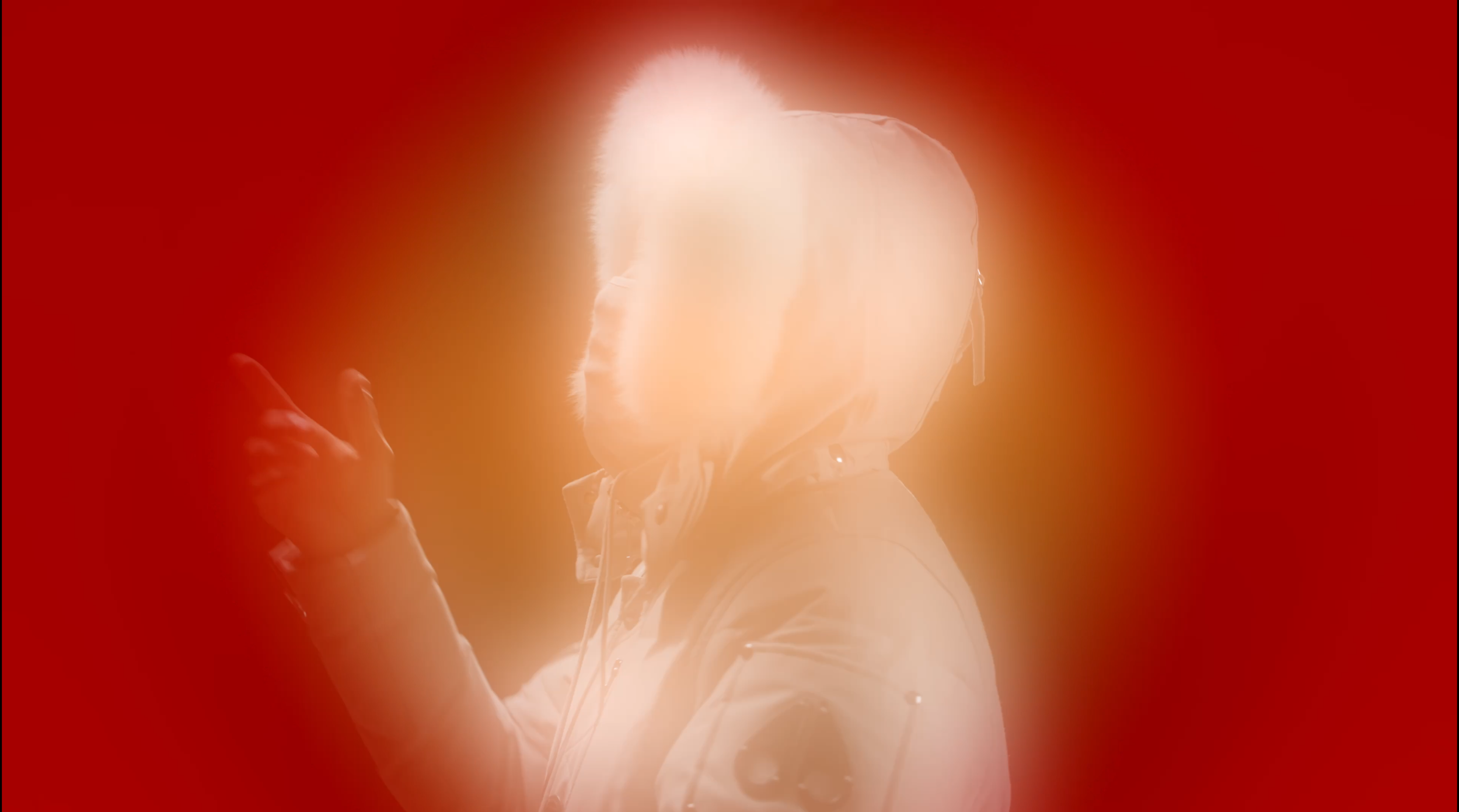 Person wearing a space helmet and a jacket, with a bright, glowing light reflecting off the helmet, surrounded by a red background.