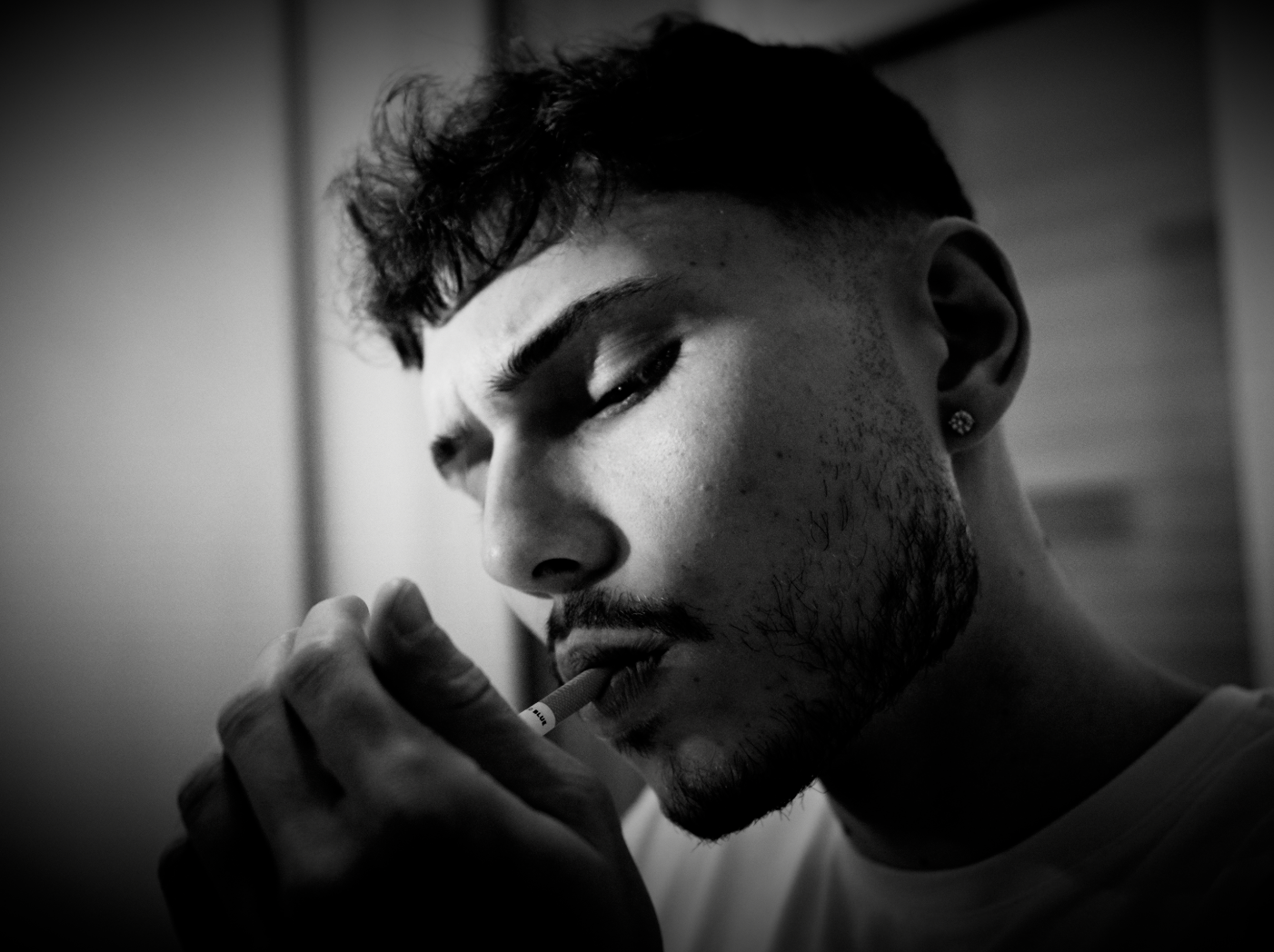 Close-up of a man with a beard and short hair, smoking a cigarette, looking down with a serious expression, in black and white.