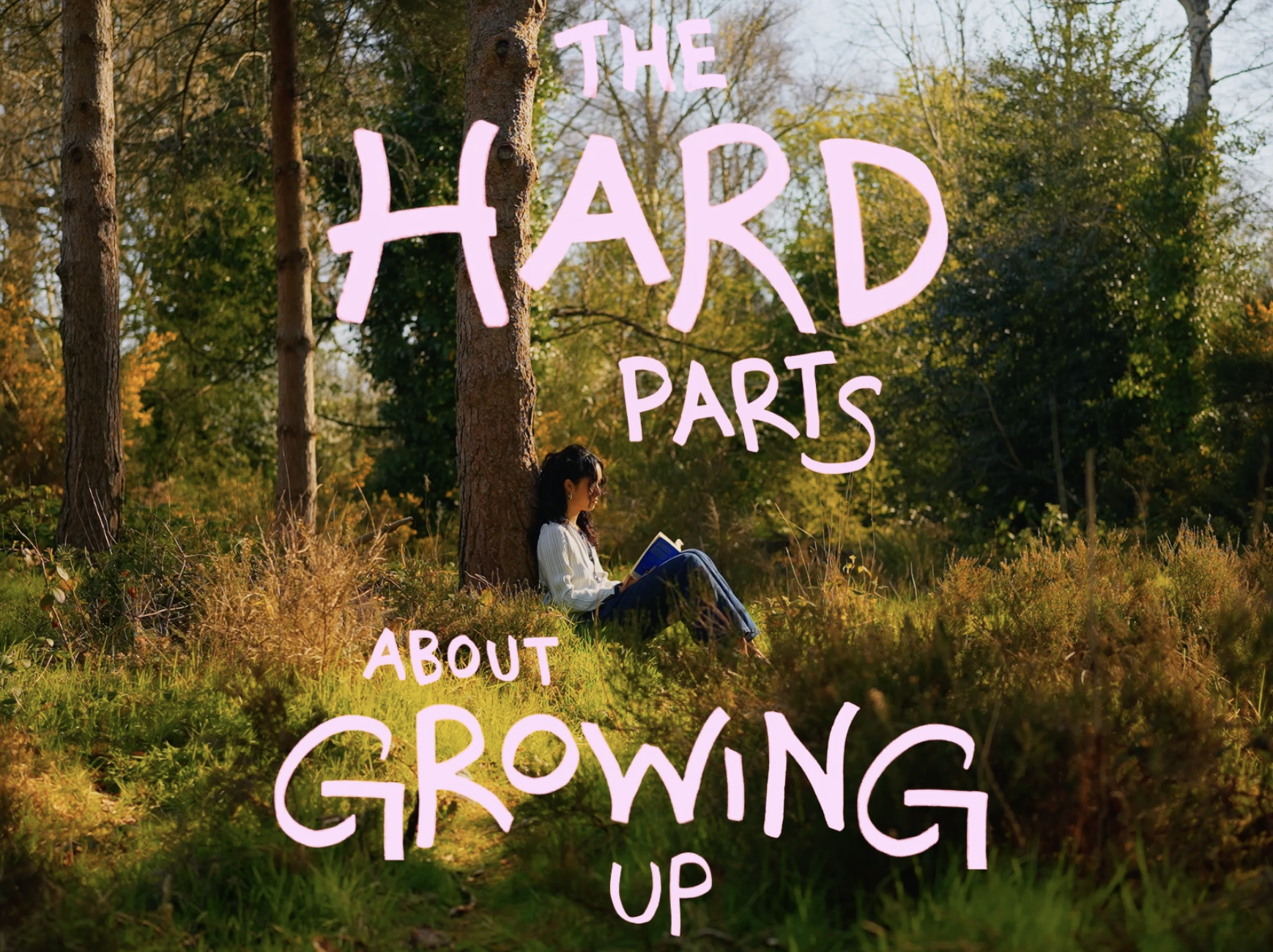 A woman sitting against a tree in a forest reading a book, with overlaid pink text saying, 'The hard parts about growing up.'
