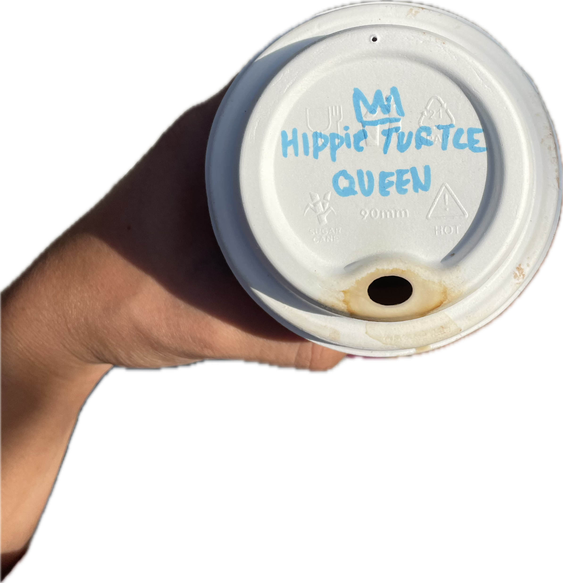 Hand holding a coffee cup with the lid facing up. The lid has blue handwritten text reading "Hippie Turtleneck Queen" with a crown drawing above the text. The lid is white with some brown stains near the opening.