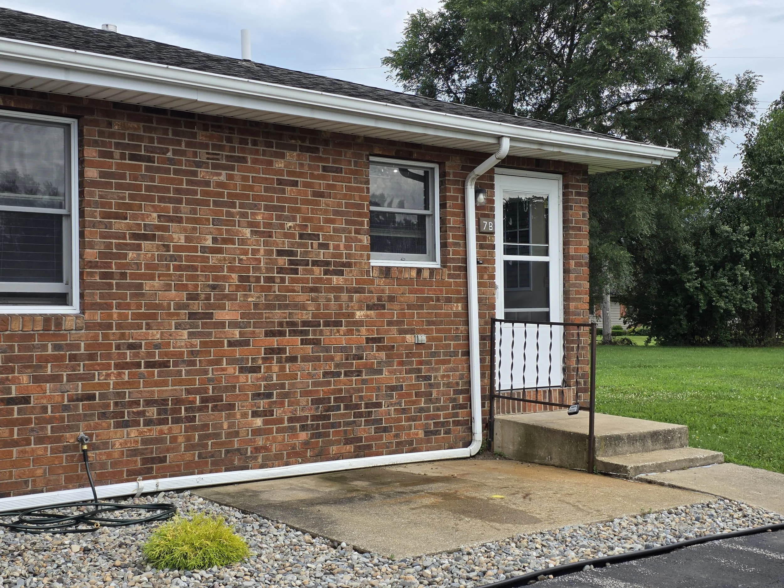 Front entrance of Unit 7B at The Vues in North Liberty, Indiana, showing the single-story brick exterior, private entry, walkway and landscaped front yard.