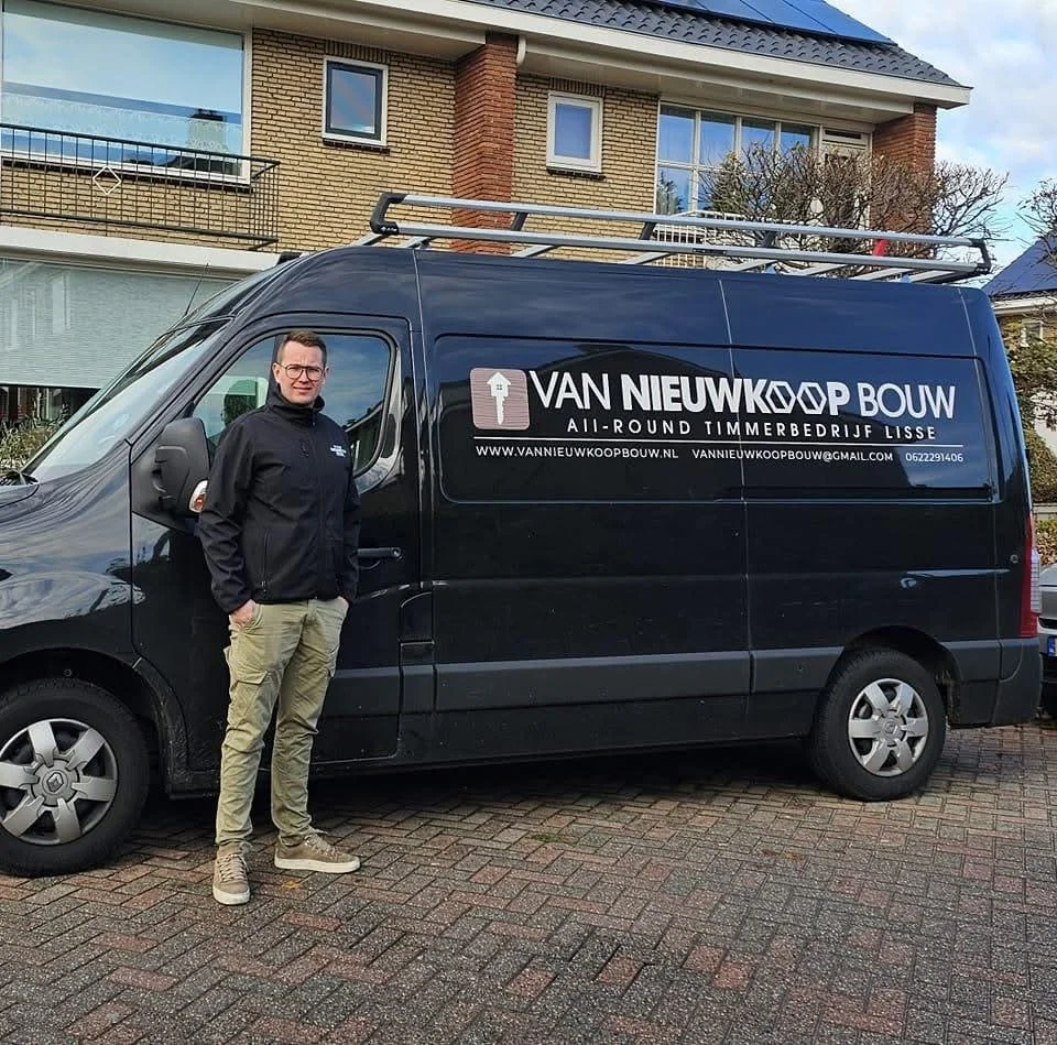 Man staat naast een zwarte bedrijfswagen met de tekst 'VAN NIEUWKOOP BOUW' en aanvullende informatie, in een woonwijk met moderne huizen.