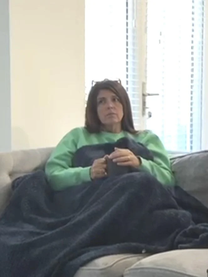 Louise Montgomery sitting on a grey sofa in a green jumper with a dark blanket over her lap.