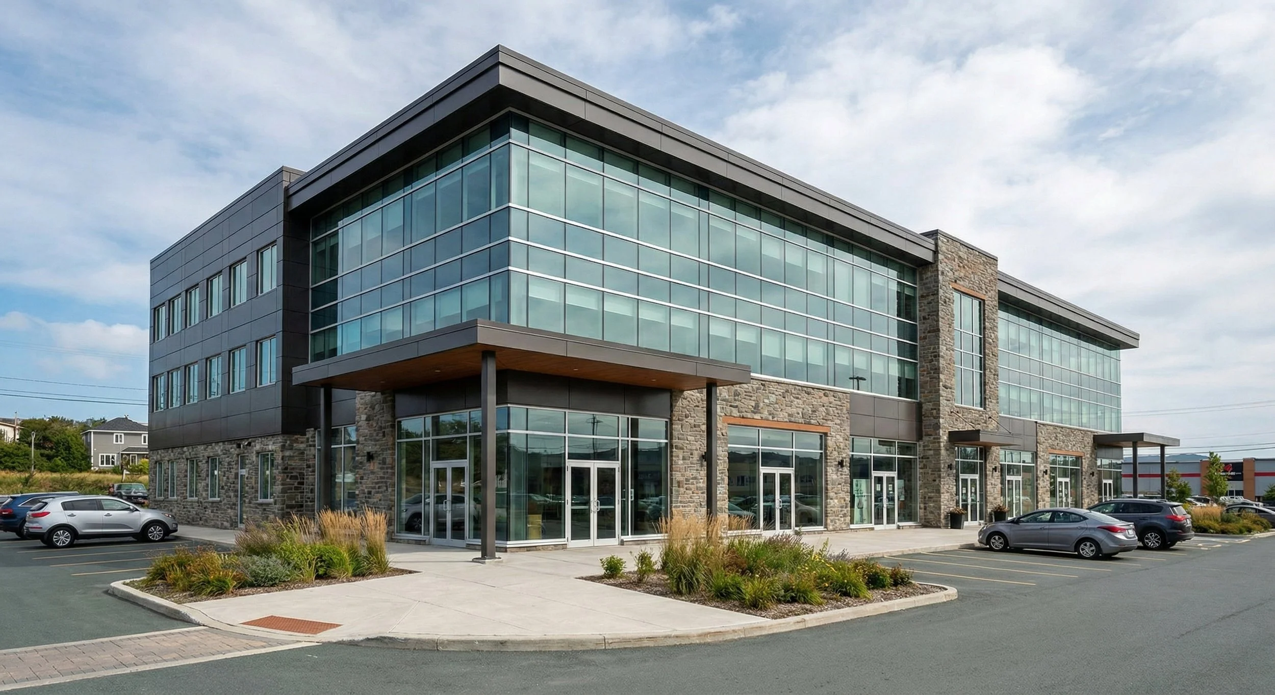 Exterior view of a modern multi-story commercial office building featuring expansive glass windows, dark metal panels, stone architectural accents, and a paved parking lot.