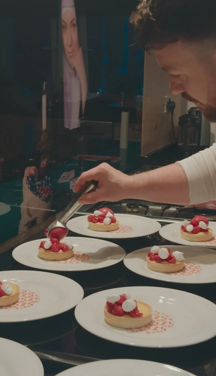 A chef using a torch to caramelize a dessert topped with berries and whipped cream on white plates.