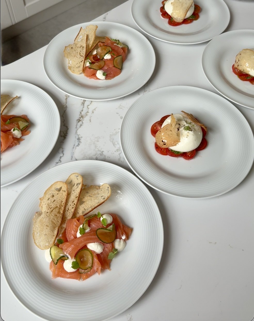 Plates of smoked salmon with capers, cream, and bread on a white table.