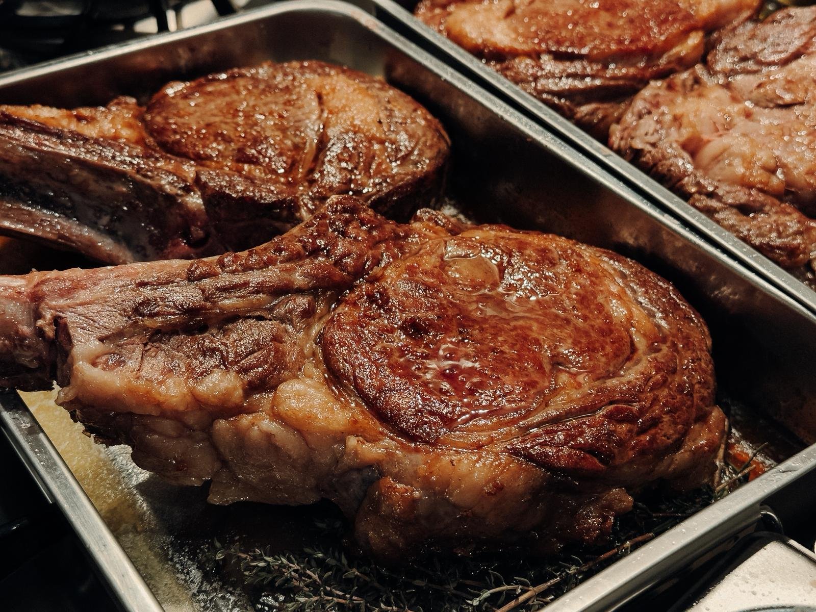 Close-up of cooked beef steaks in a metal tray.