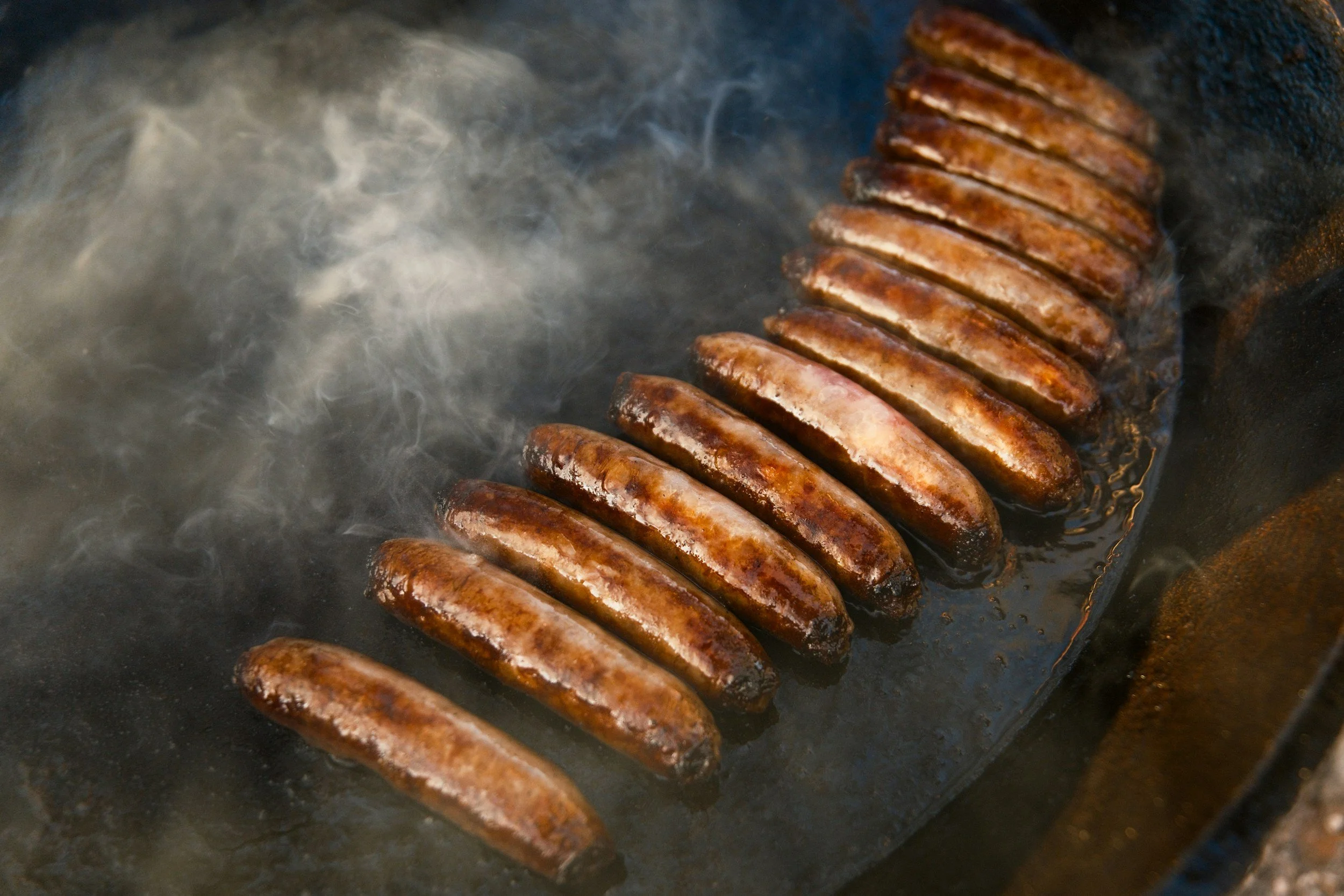 Sausages cooking on a grill or pan, with steam rising.