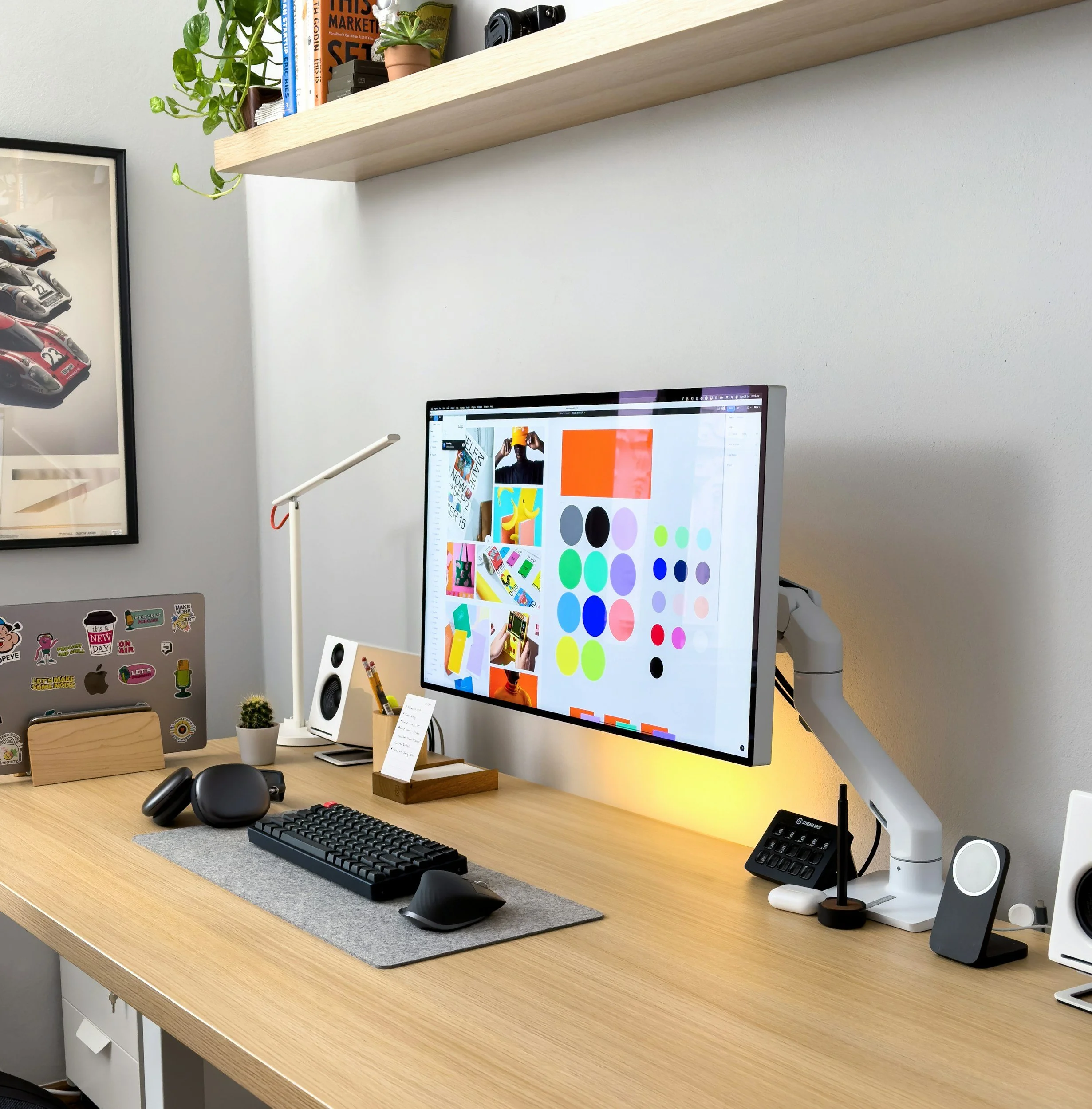 Home office desk with a computer monitor displaying graphic design ideas, a keyboard, mouse, small speaker, white desk lamp, potted cactus, headphones, and other accessories.