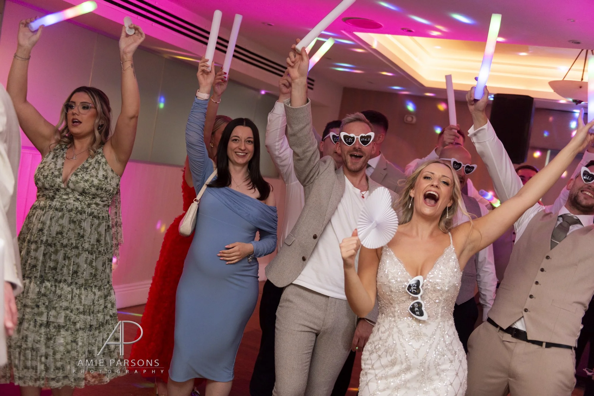 A very happy bride and groom with their guests. They have their arms in the air whilst on the dancefloor