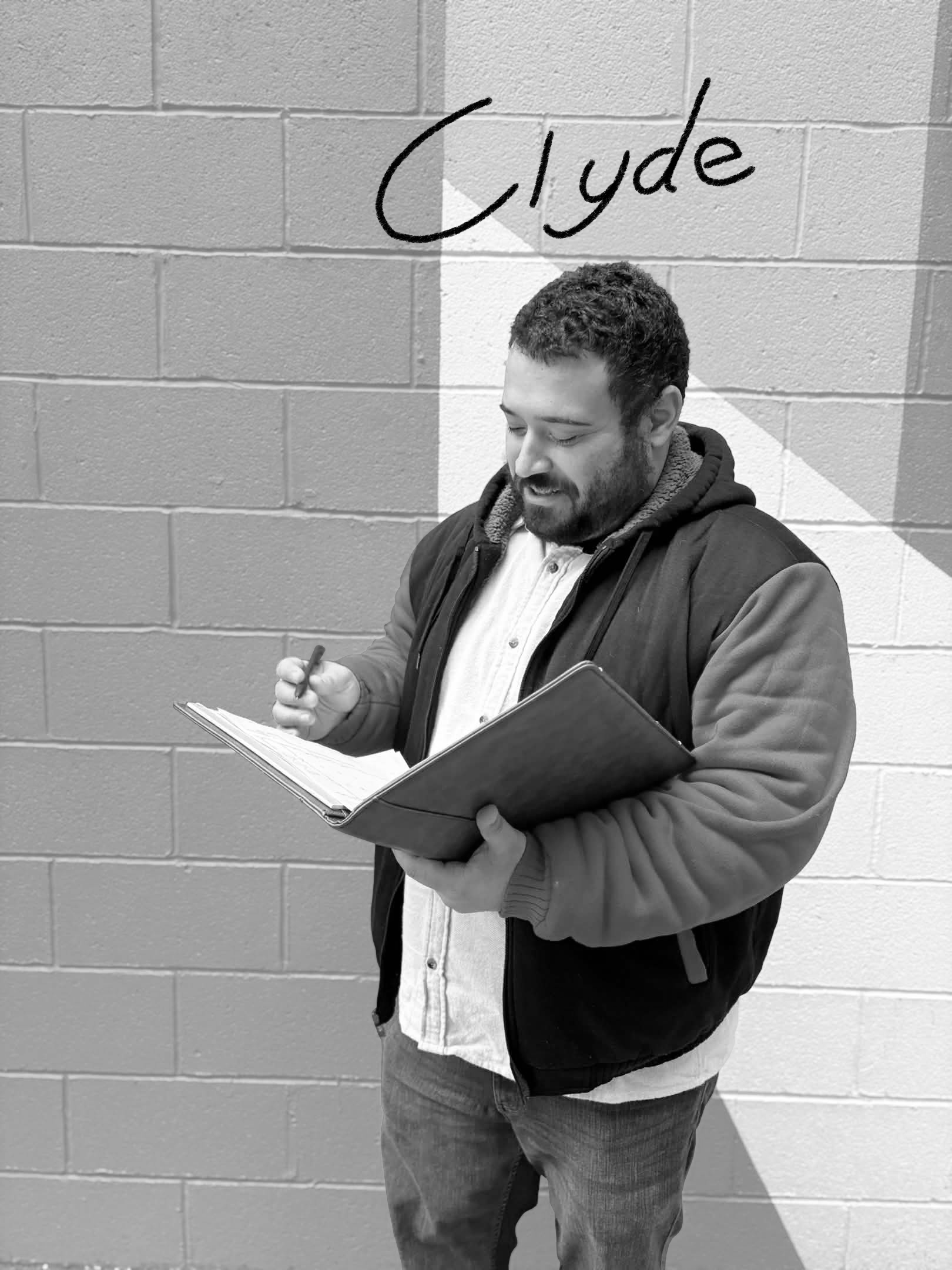 A young man with a beard and curly hair standing against a brick wall, writing in a notebook, with the name 'Clyde' written above his head.