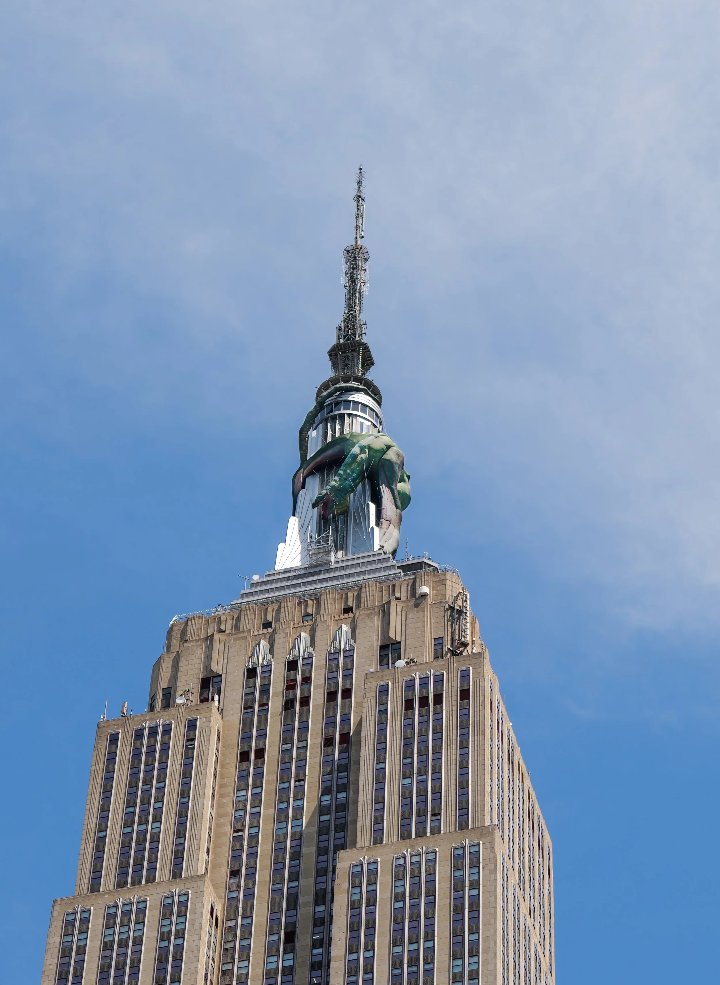 The Empire State Building with a large dragon sculpture attached to its upper section, set against a clear blue sky.