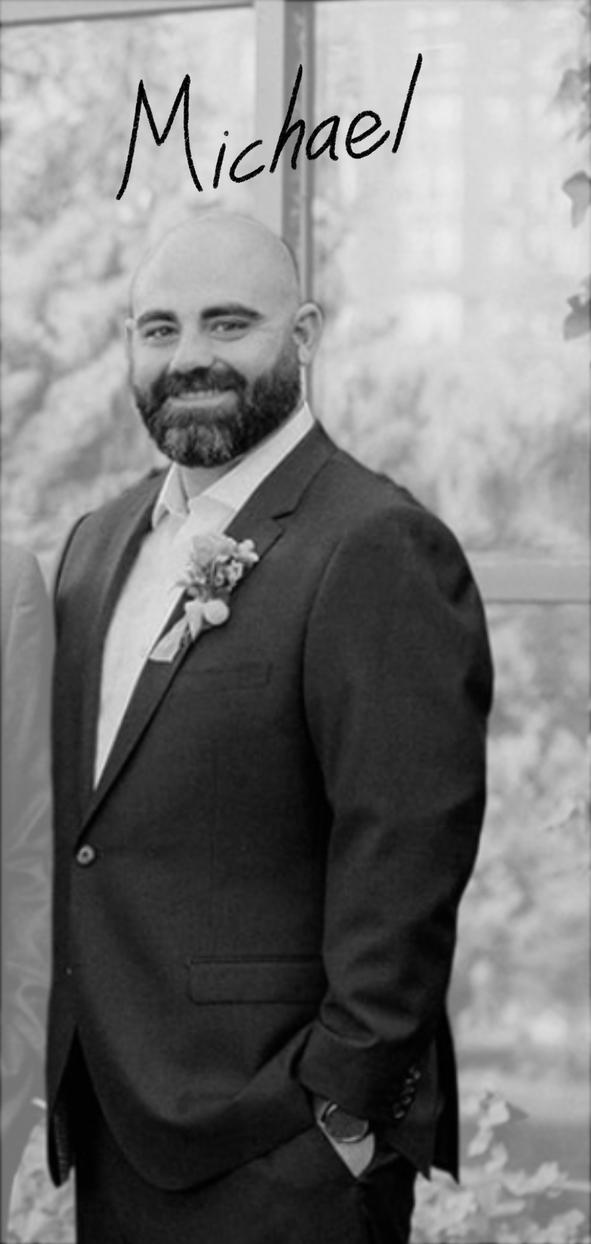 Aa man in a suit with a boutonniere, standing outdoors.