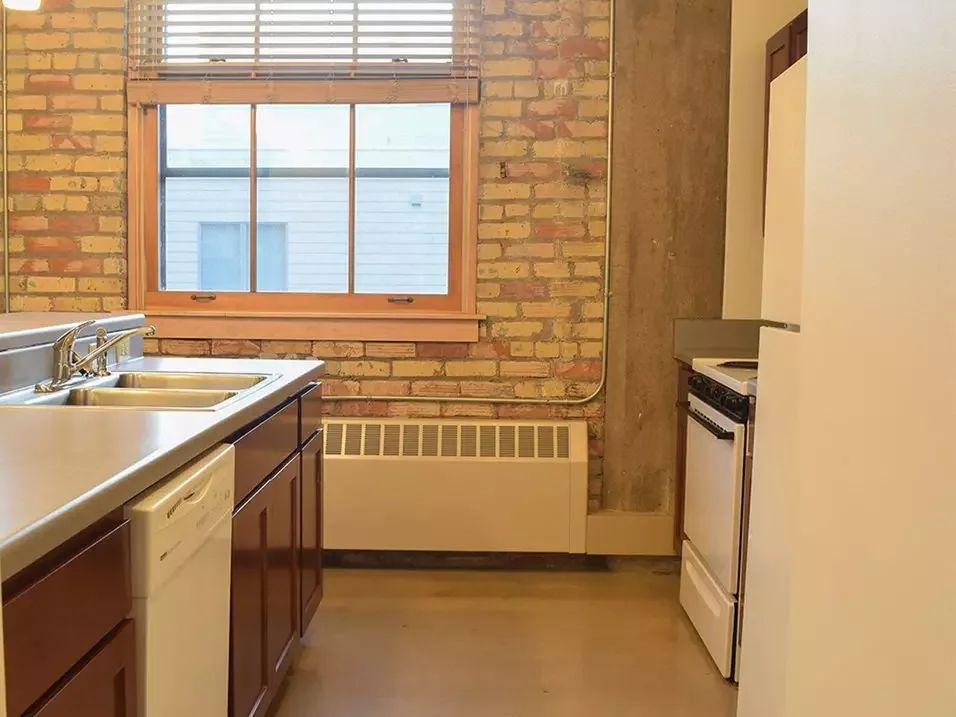 Small kitchen with brick wall, a window, a double sink, dishwasher, stove, and a refrigerator.