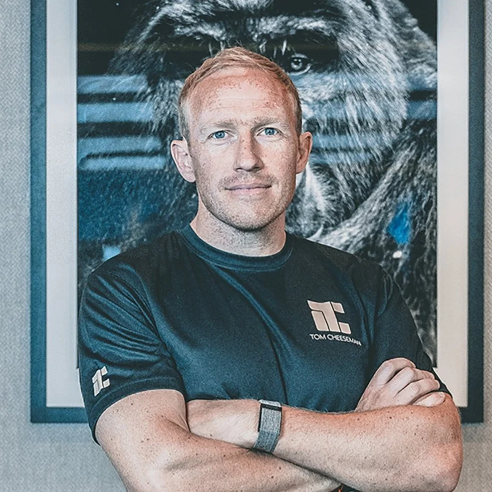 A man with crossed arms standing in front of a framed photograph of a dog and a wolf.