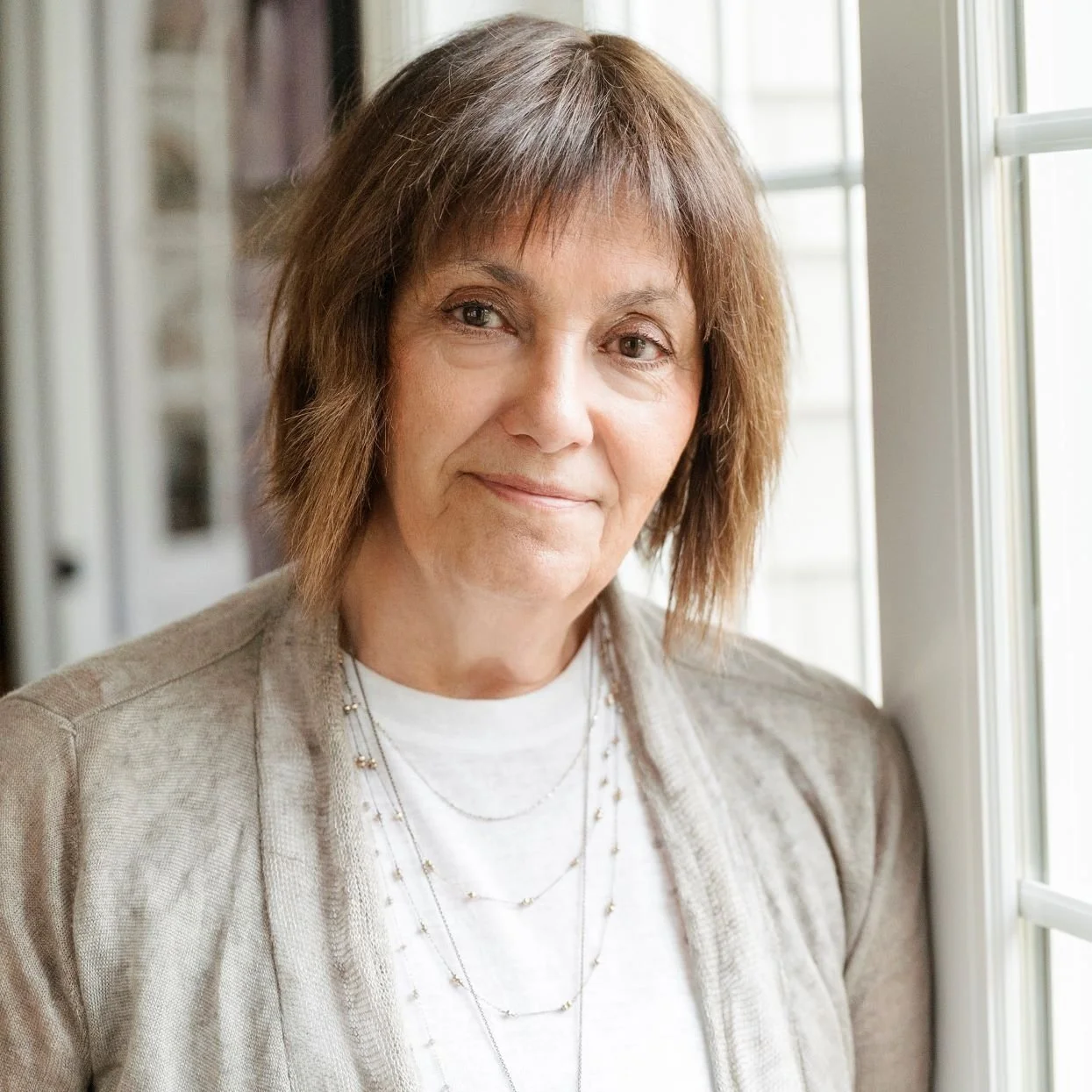 A middle-aged woman with short brown hair standing indoors near a window.