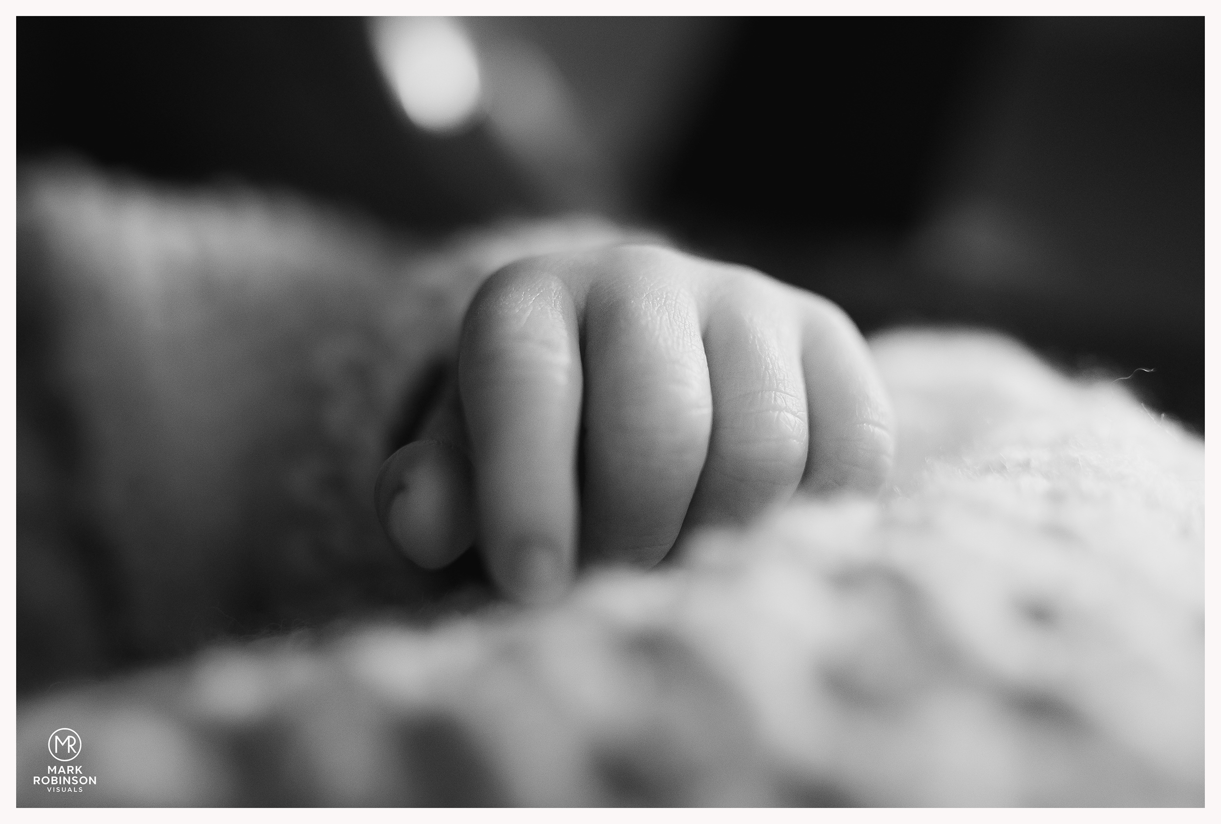 Close-up of small baby hand gripping an adult finger, black and white photography.