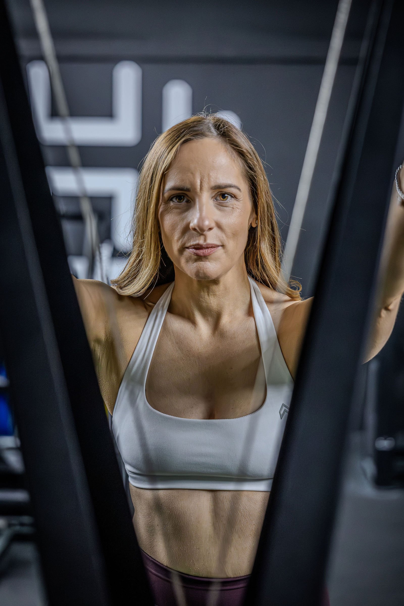 Fitness woman in sportswear looking upward during workout, seen through gym equipment.