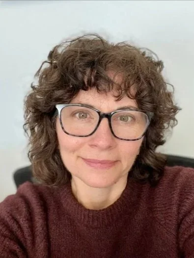 The author with curly brown hair and glasses smiling at the camera.