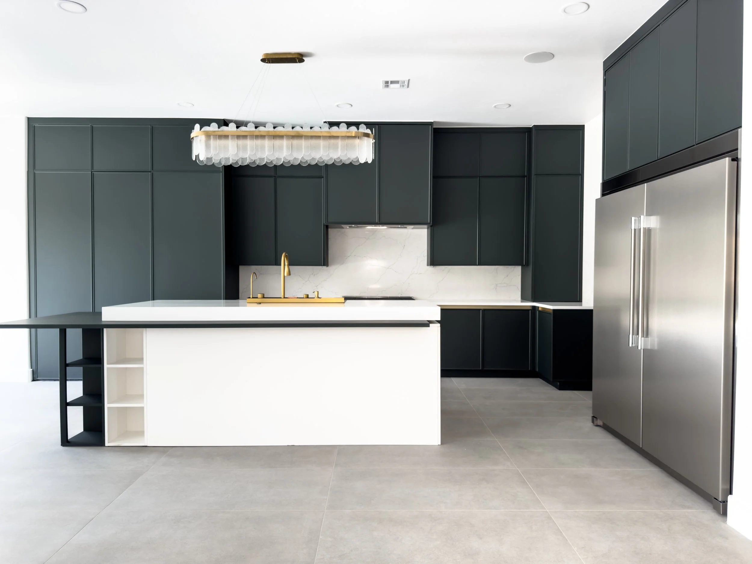 Modern kitchen with dark cabinets, marble backsplash, and a white island with black shelving, gray flooring, and a large refrigerator.