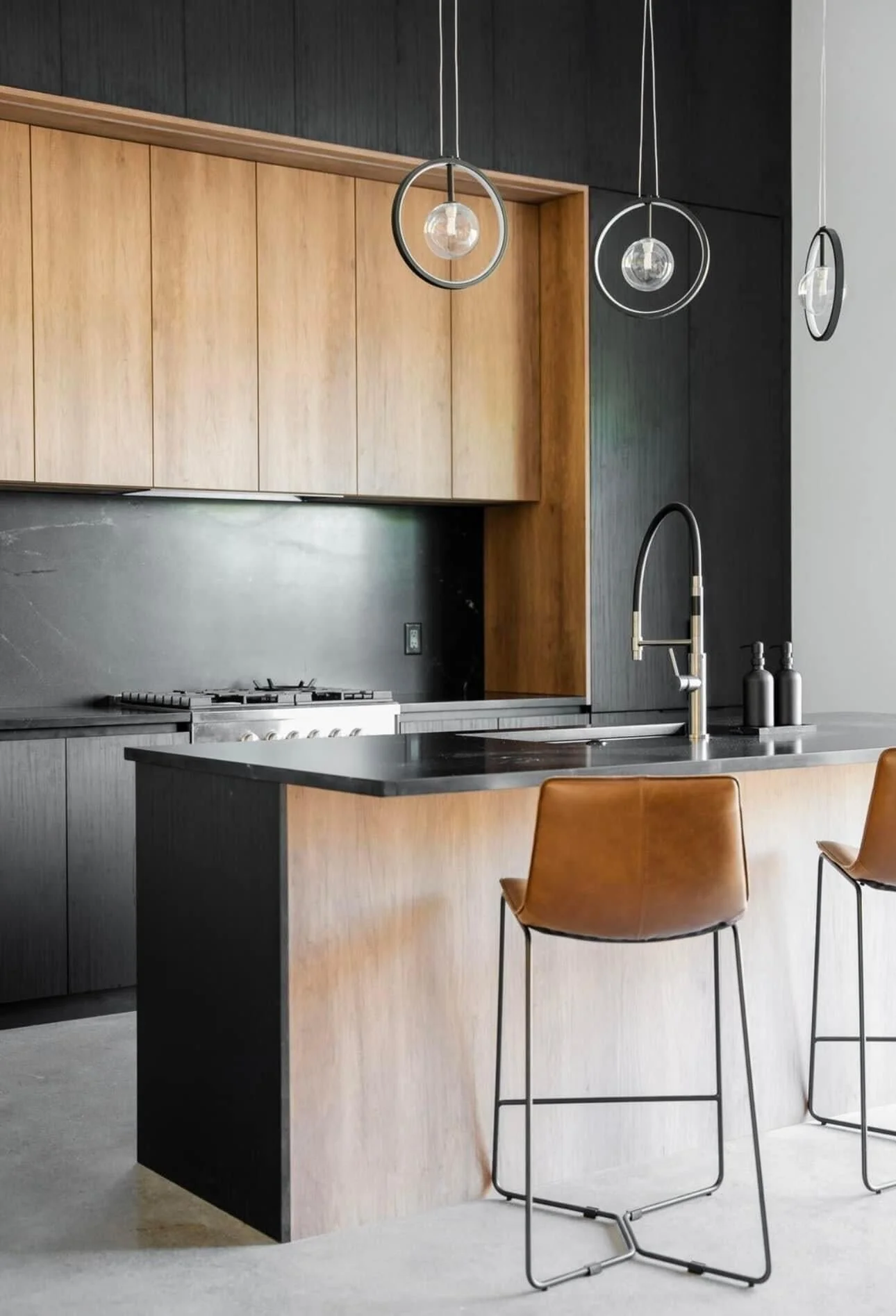 Modern kitchen with black and wood cabinetry, a stainless steel stove, a black kitchen island with a wood finish, a black faucet, and two brown chairs with black metal frames.