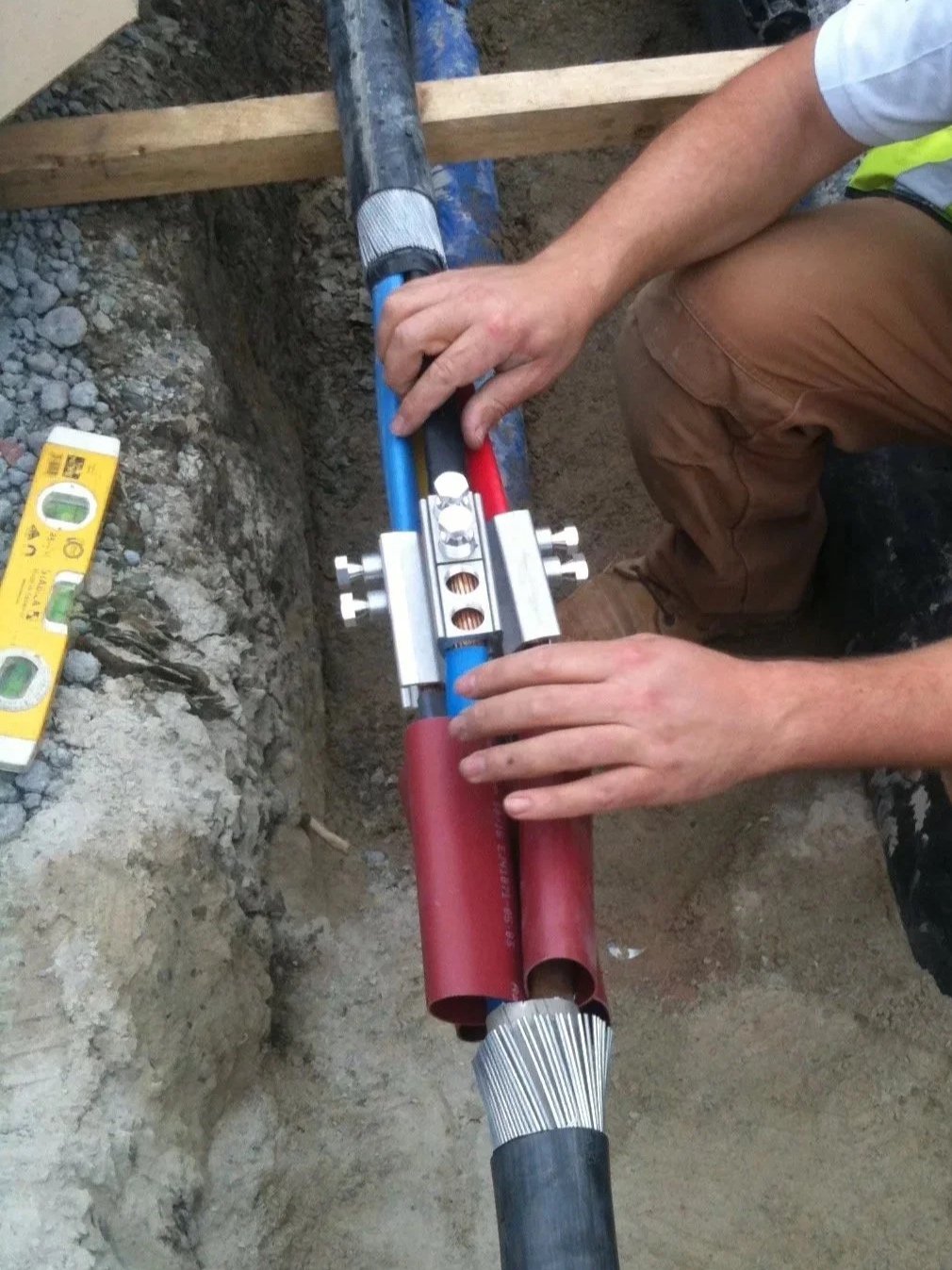 A worker installing or repairing underground piping with a specialized pipe fitting tool, using red and blue pipes in a construction site.