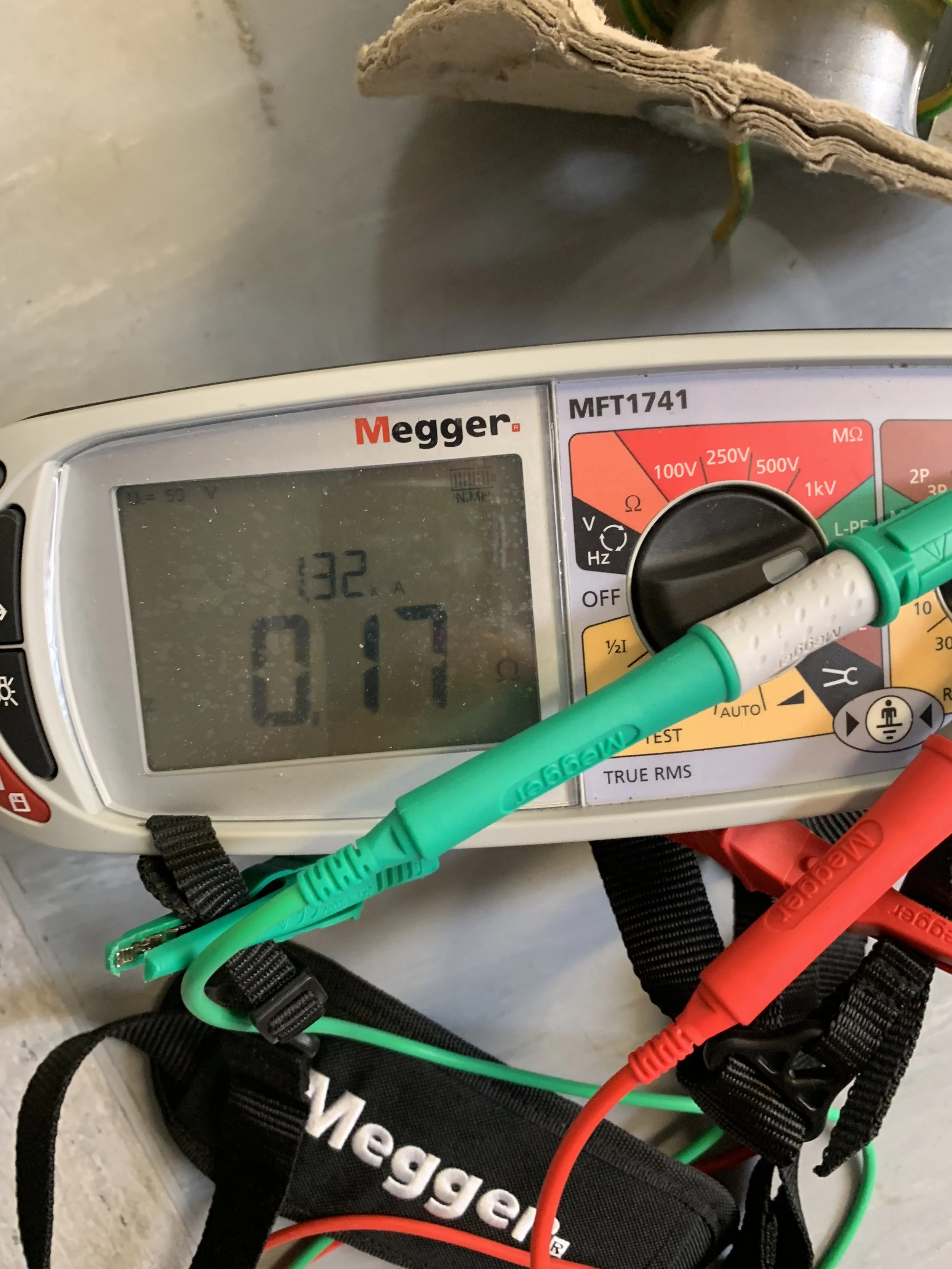 A Megger digital insulation tester showing a reading of 17 ohms. Test leads are connected, with one green and one red, and a black strap with the Megger logo is also visible.