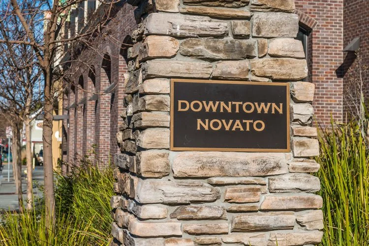 A stone pillar with a black sign reading "Downtown Novato" is visible, with buildings and trees in the background.