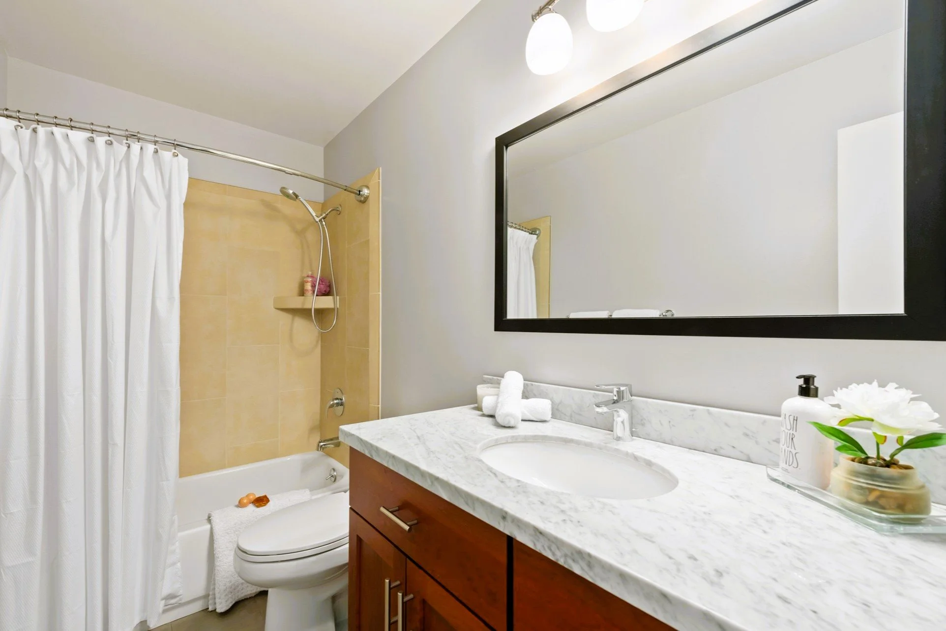 Bathroom with a vanity, a large mirror, a sink, a marble countertop, a wooden cabinet, a toilet, and a shower with a white curtain and beige tiles.