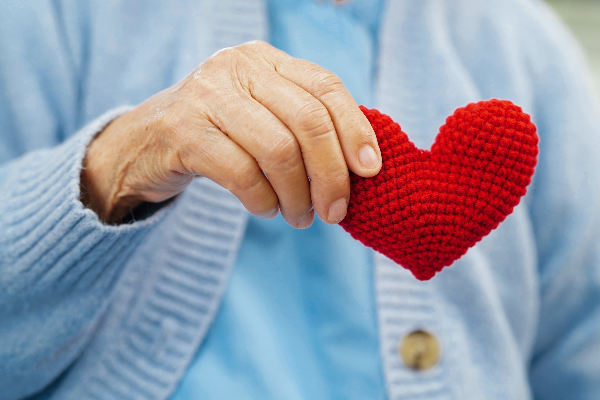 Close-up of an older adult's hand holding a small red knitted heart.