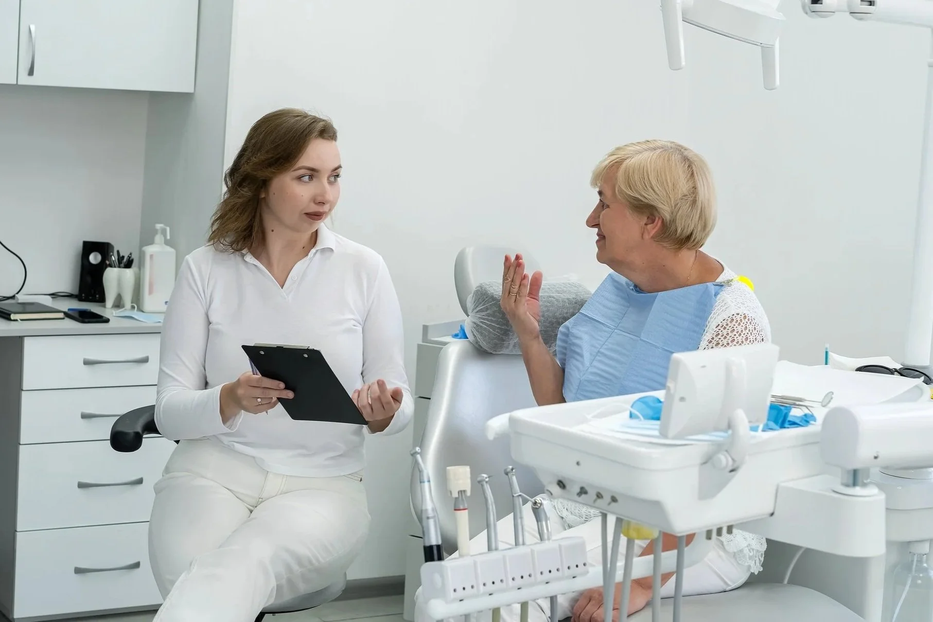 A female healthcare professional with a clipboard talking to an elderly woman in a dental clinic.