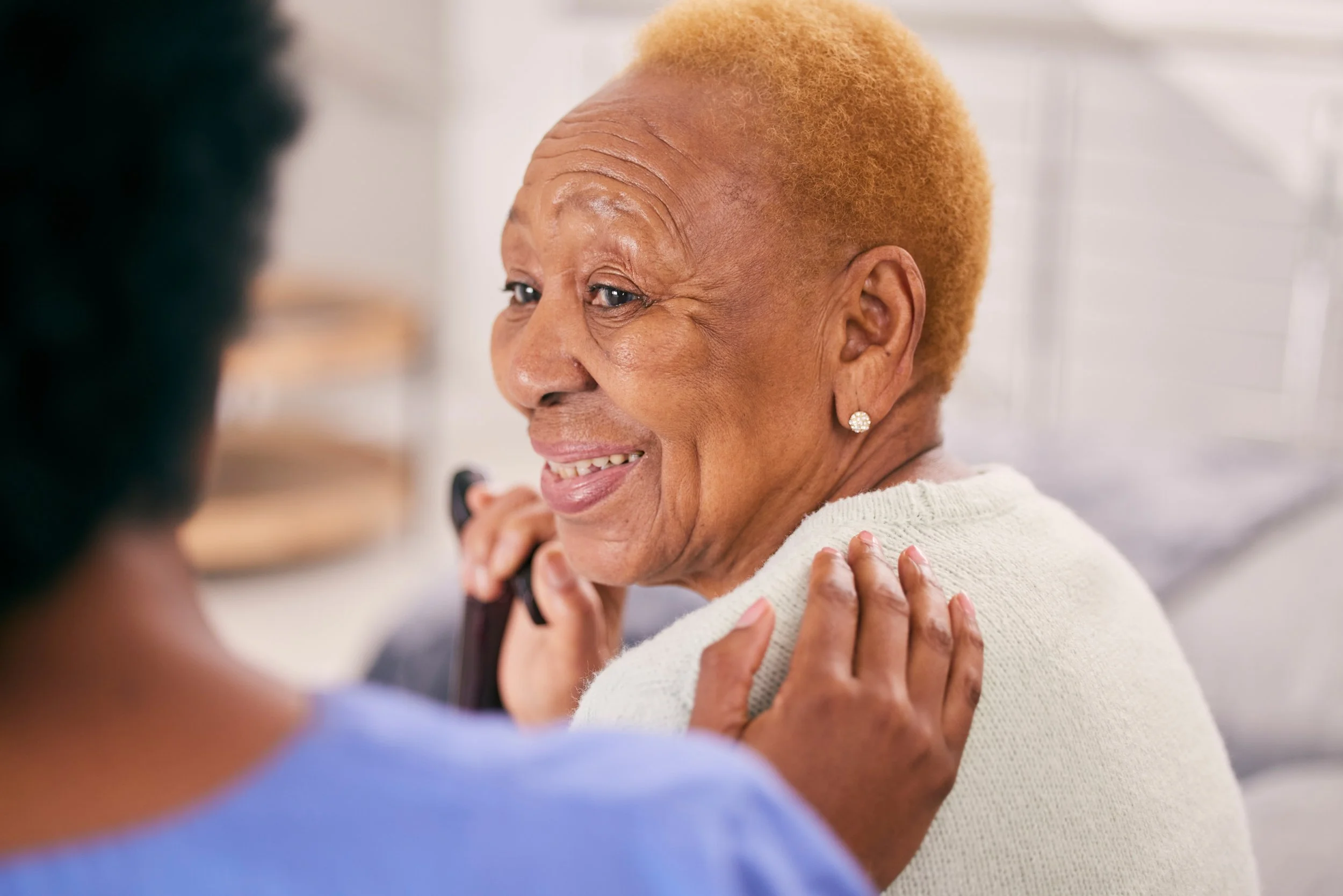 Older adult smiling while talking on the phone with a supportive person nearby.