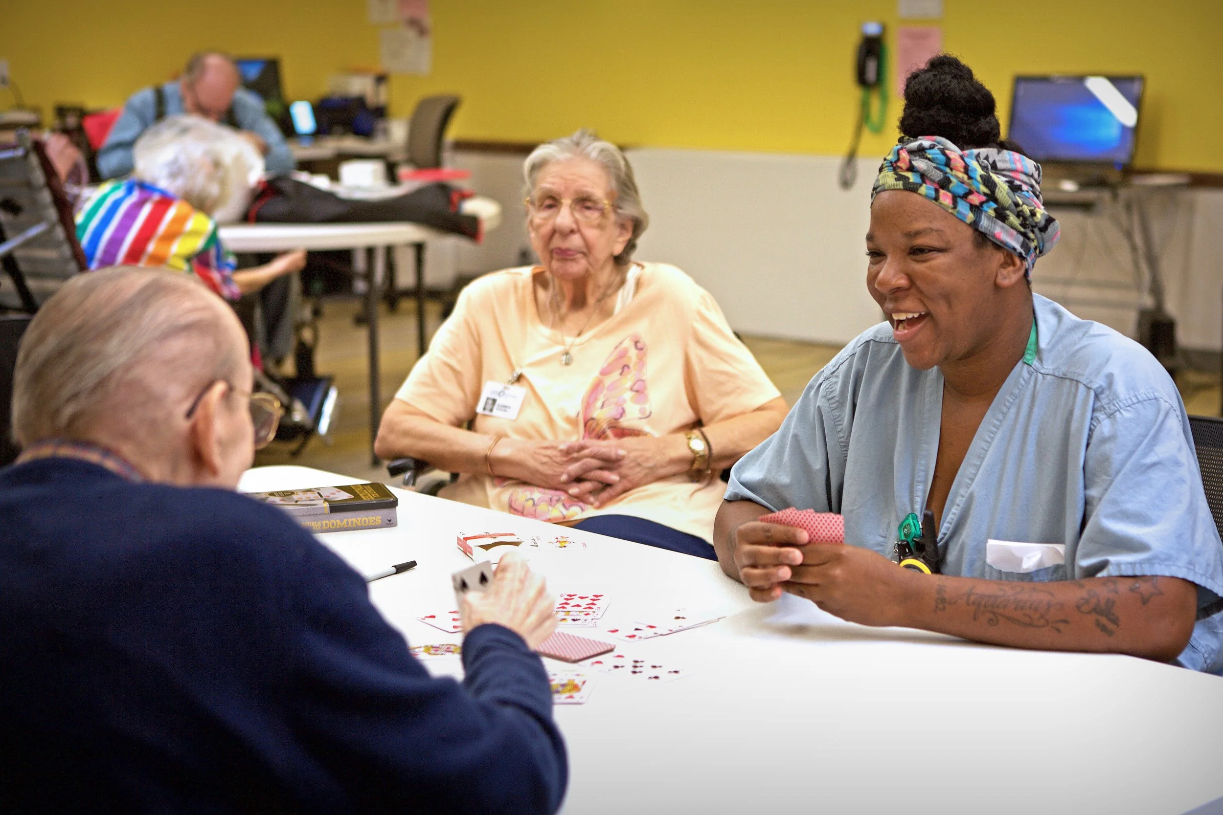 Group of diverse people playing cards and socializing at a table in a recreational center.