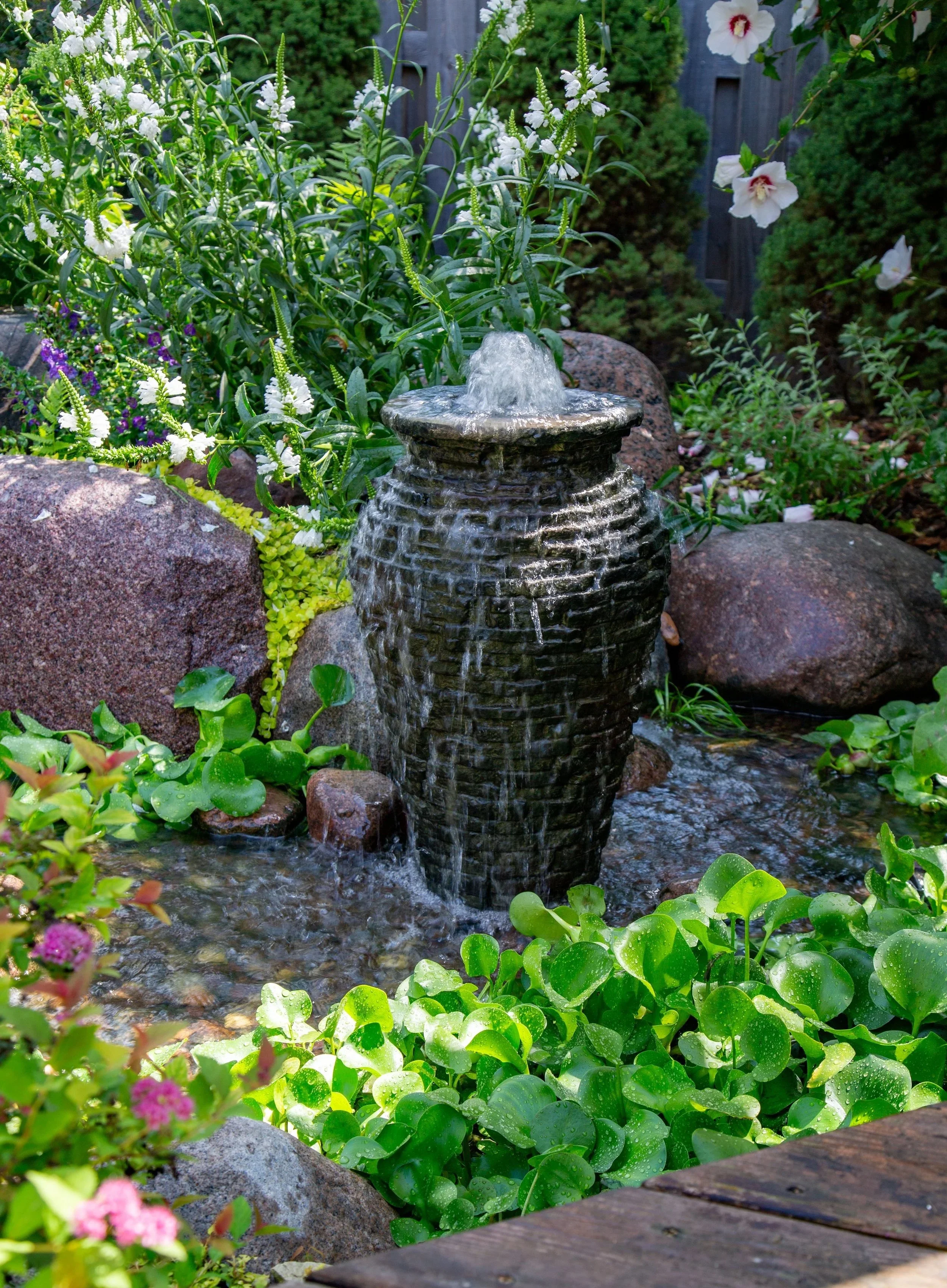 A small waterfall fountain surrounded by lush green plants and rocks in a garden.