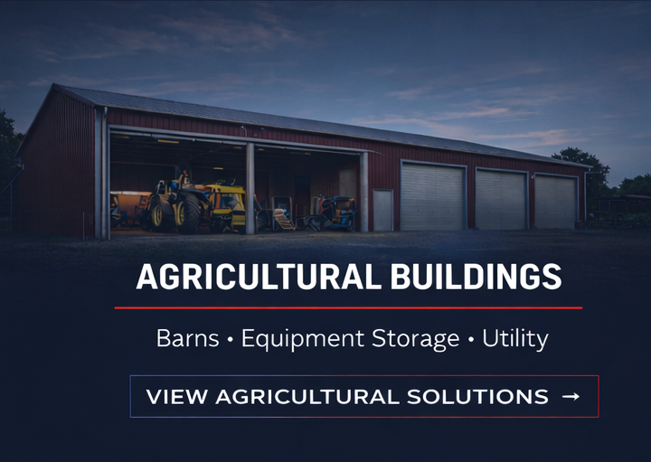 An agricultural storage building with a red metal exterior, multiple garage doors, and farming machinery parked outside during dusk.