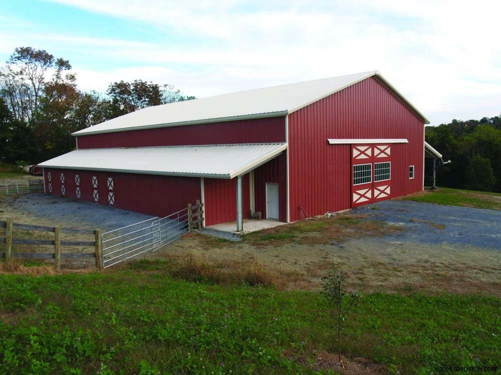 Red barn with white roof and trim, surrounded by green grass and trees in the background.