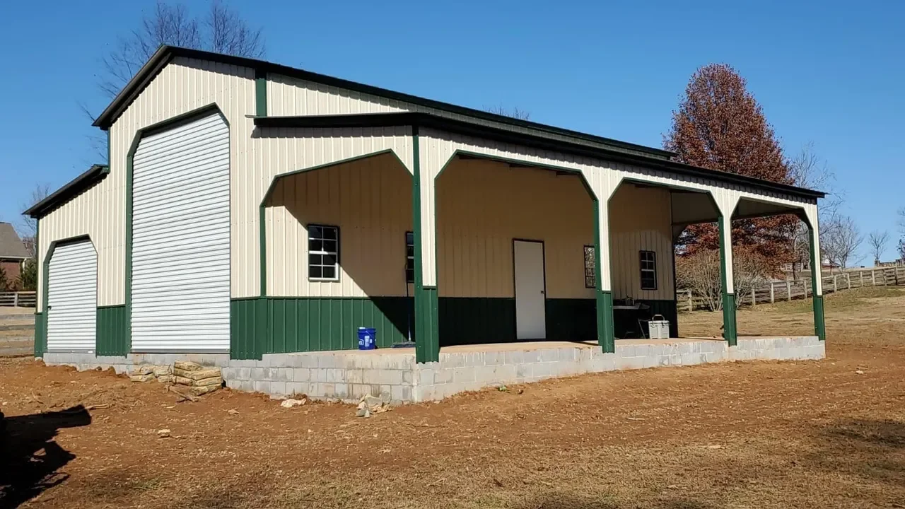 A large metal storage building with two roll-up doors and a small side door, built on a concrete block foundation, with a dirt yard in the foreground and trees in the background.