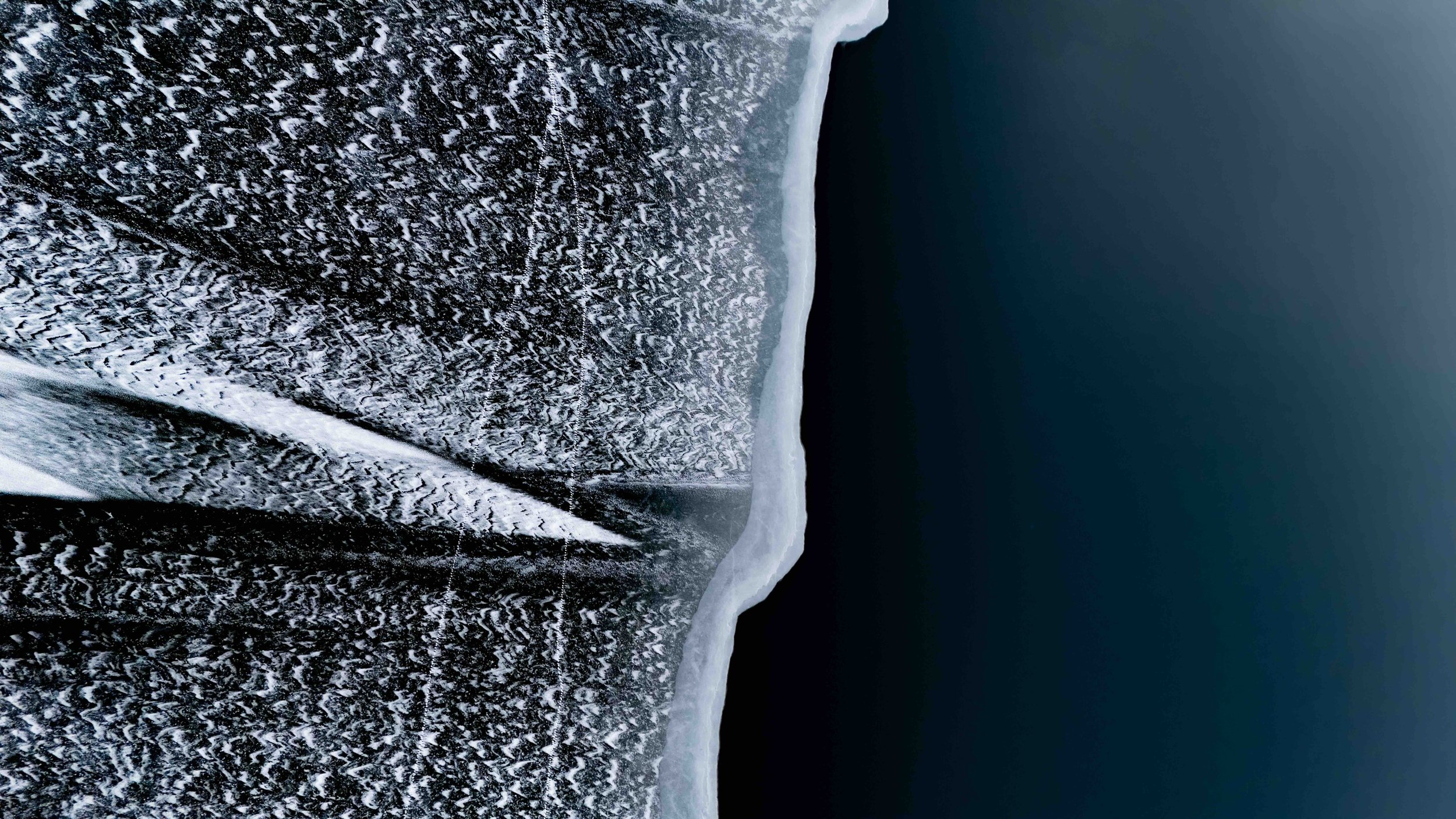 Close-up of a frozen, snow-covered surface with a dark, calm body of water in the background.