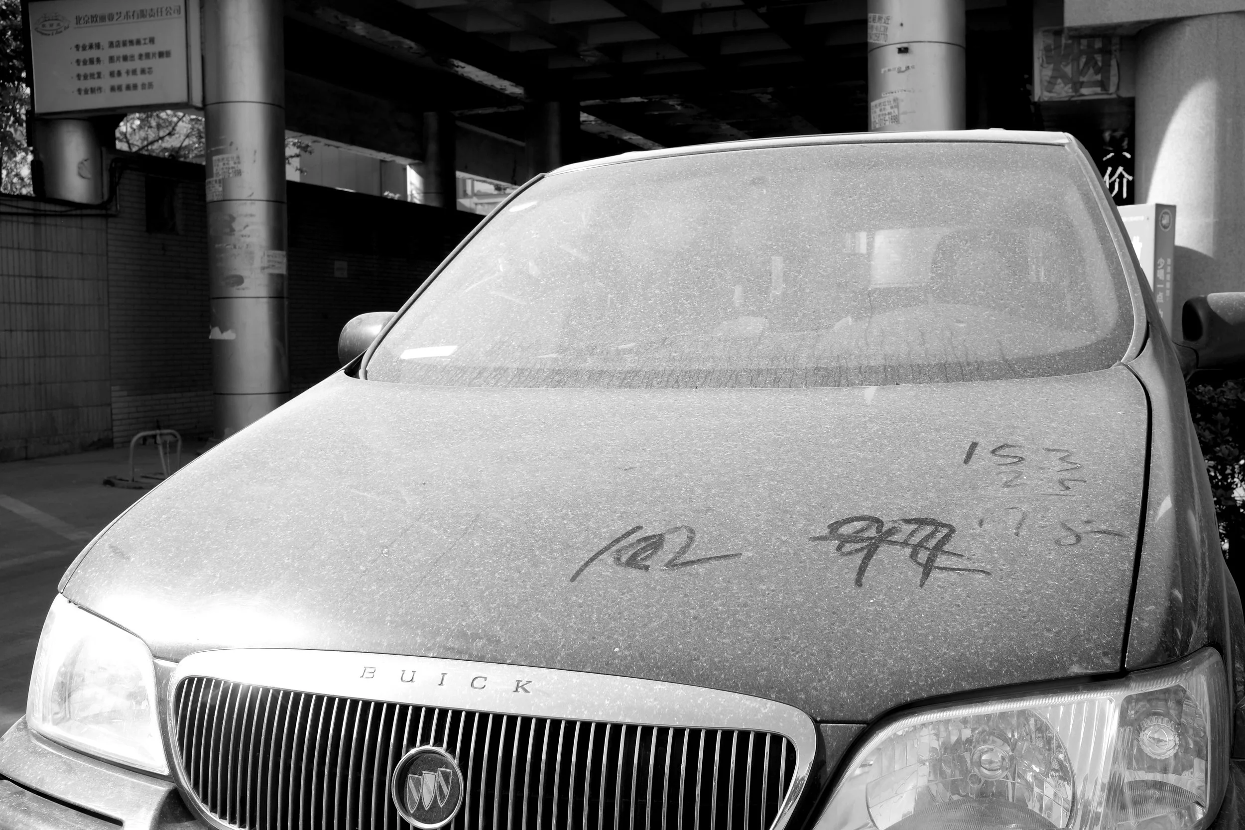 Minimalistisches Stillleben in Peking: Ein dick eingestaubtes Auto, auf dessen Motorhaube Schriftzeichen hinterlassen wurden. Pvre u nutzt hartes Licht, um die Textur des Staubes und die grafischen Linien als urbanes Kunstwerk hervorzuheben.