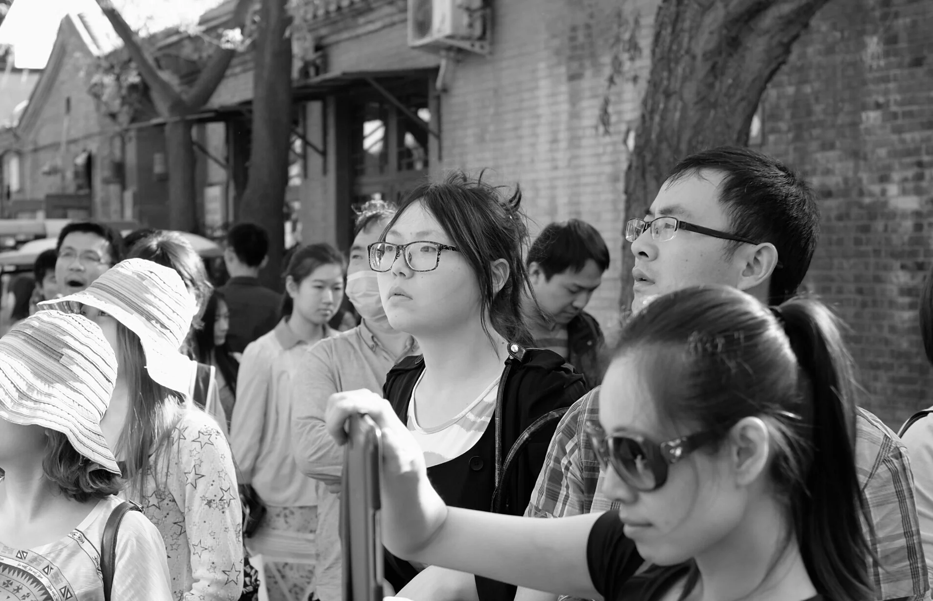 Beobachtung einer wartenden Menschenmenge in einer Pekinger Straße. Die selektive Schärfe lenkt den Blick auf die individuellen Gesichtsausdrücke und Brillendetails, während der Hintergrund in weicher Unschärfe verschwimmt – Charakterstudie von pvre 