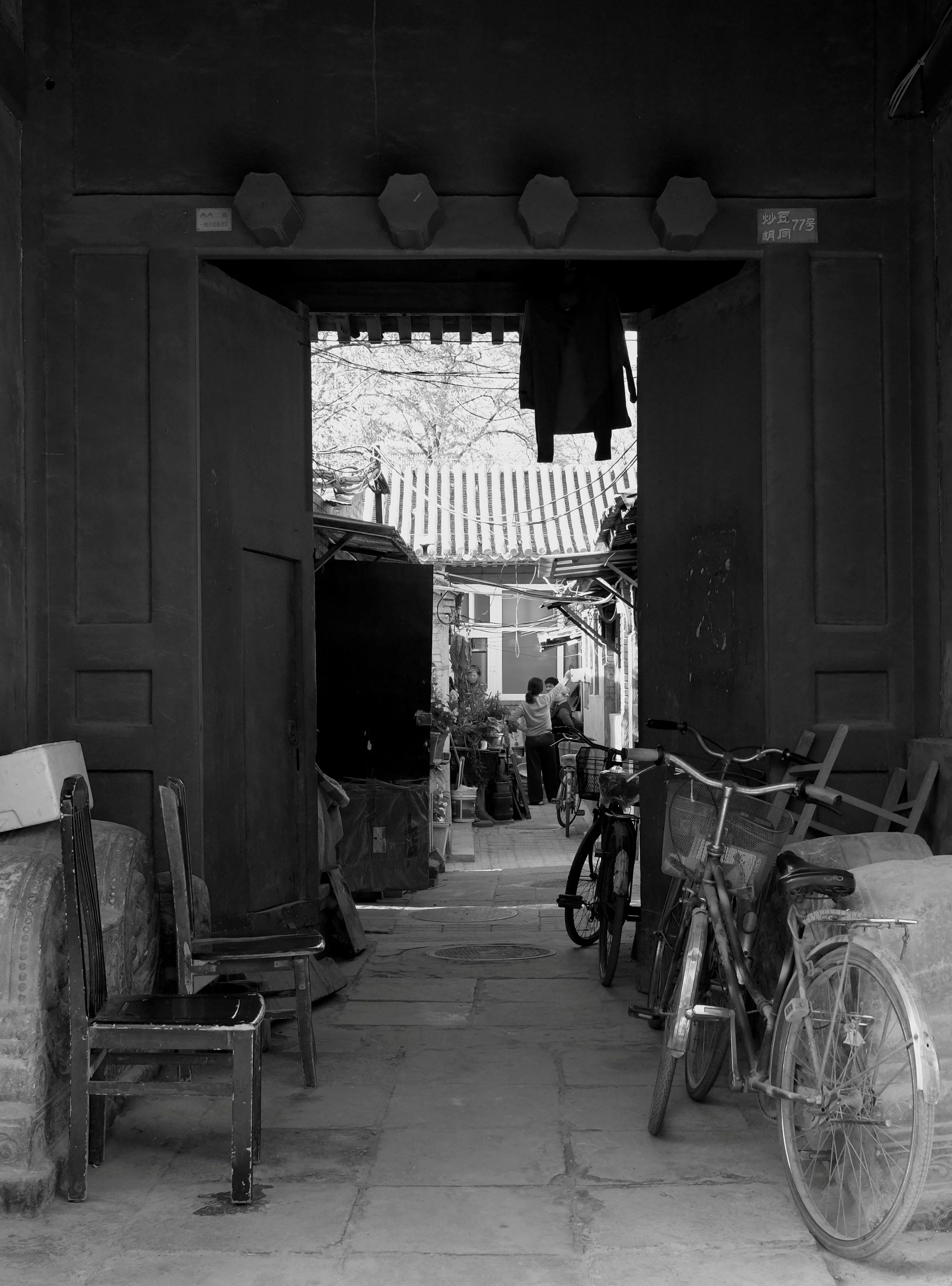 Blick in einen authentischen Pekinger Hinterhof (Hutong) mit abgestellten Fahrrädern und Alltagsgegenständen. Natürliches Licht flutet durch den Torbogen und schafft eine dokumentarische Tiefe. Pvre u zeigt das ungeschönte, echte Leben in den Straßen