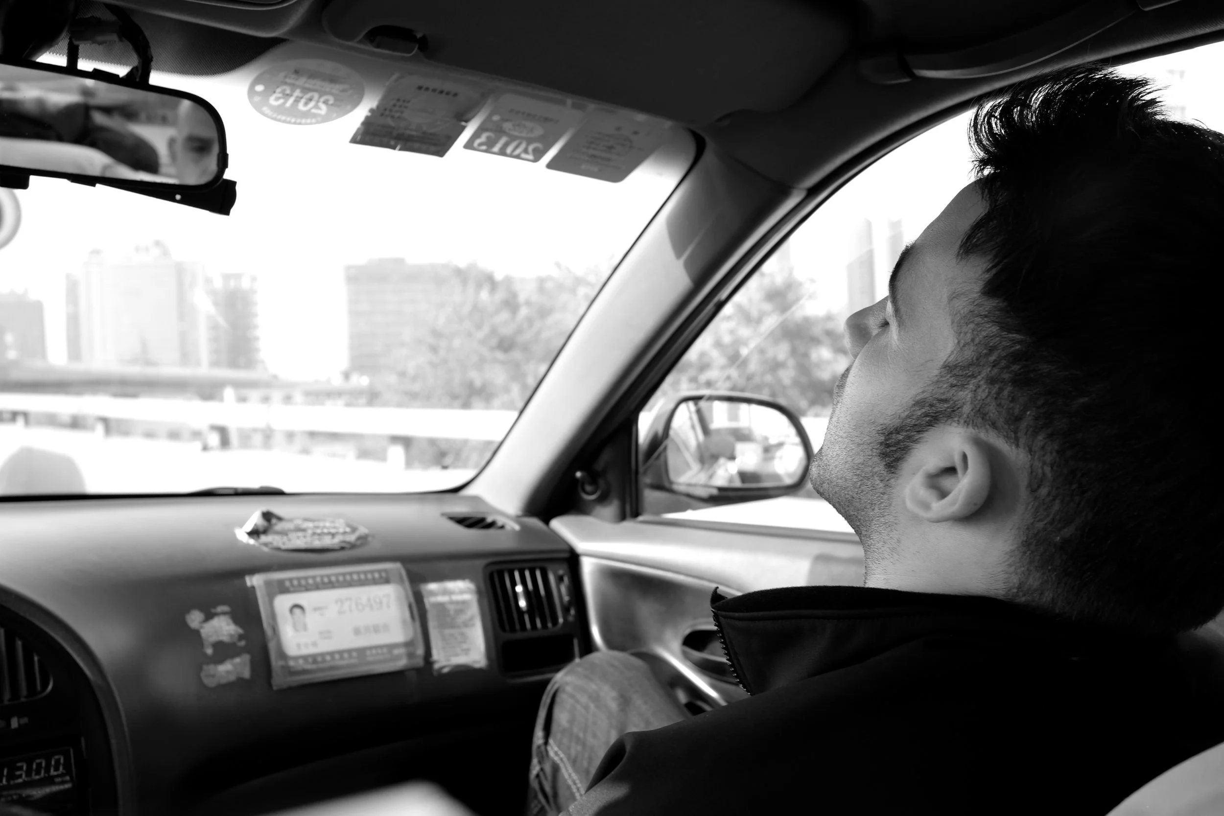 Intimes Porträt in einem Pekinger Taxi: Ein junger Mann lehnt sich entspannt zurück, während das Stadtbild im Fenster vorbeizieht. Fokus auf das Spiel zwischen Innenraum-Details und hellem Außenlicht – authentisches Visual Storytelling von pvre u.