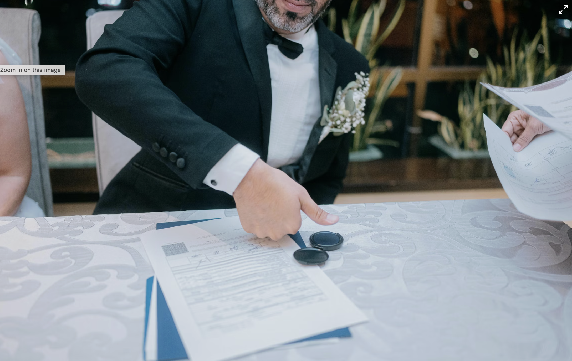 Man in tuxedo with boutonniere signing a document at a wedding reception.