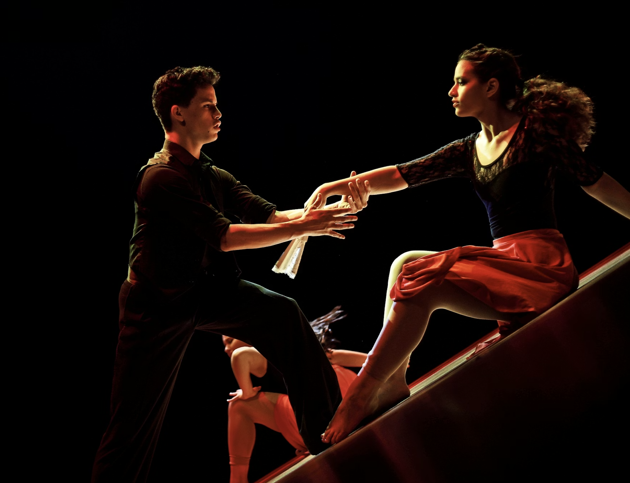 Two ballet dancers performing on stage, one male and one female, with a third dancer partially visible in the background.